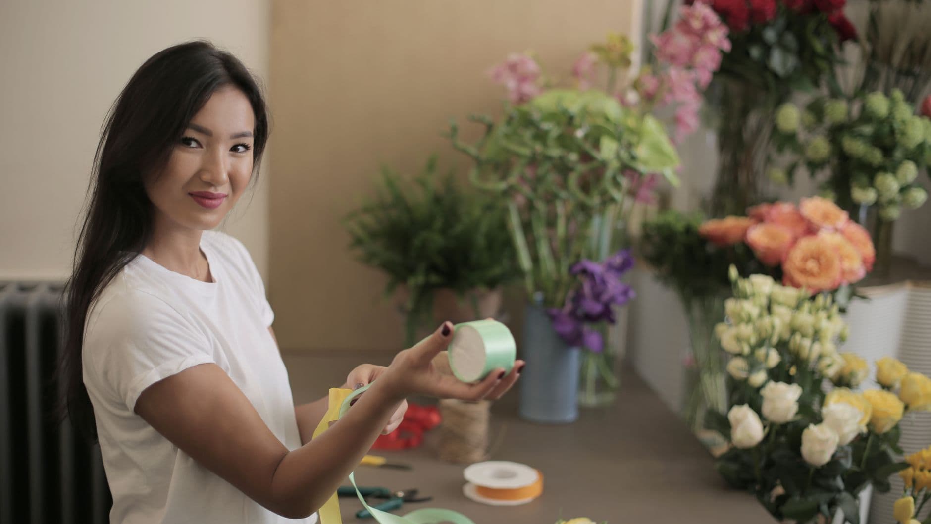 A florist standing at her workbench with reels of ribbon, surrounded by buckets of cut flowers